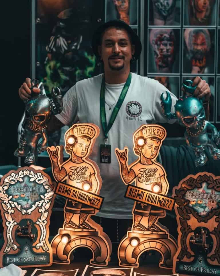 Tattoo artist (Juan Muriana) holding two awards at a tattoo convention