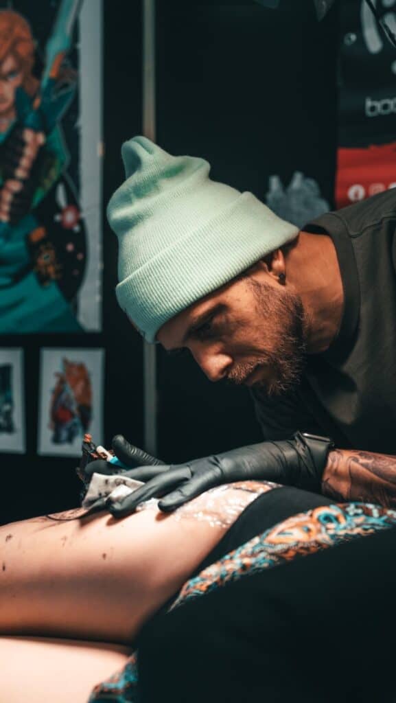 Tattoo artist with a beanie tattooing someone's thigh