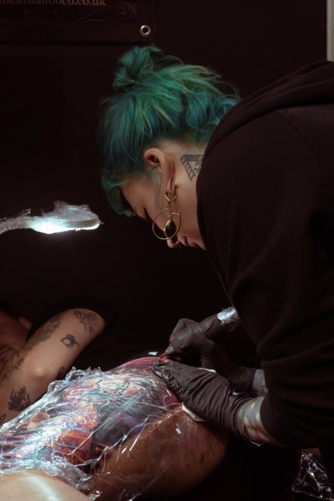 Woman with green hair tattooing a leg.