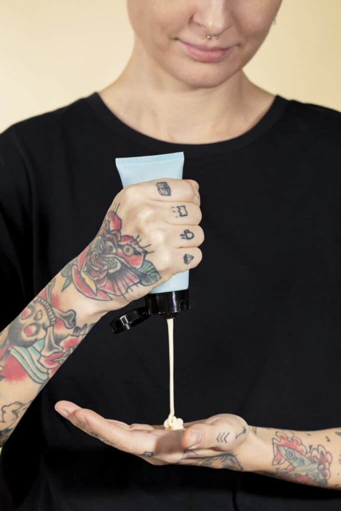 Tattooed woman squeezing cream from a blue tube